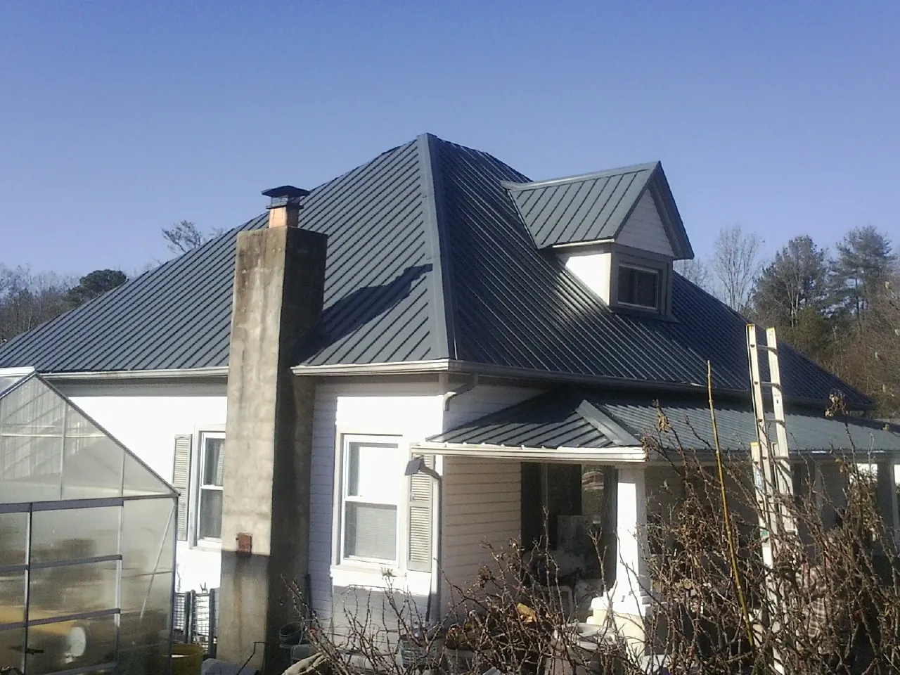 Dark blue standing seam metal roof on a white farmhouse with dormer — Slate & Tile Roof Repair by Roofing Brothers in Irving