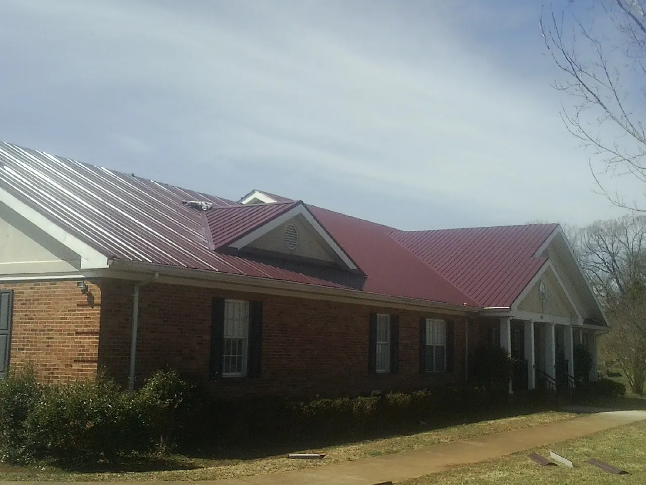 Red metal roof with gabled entries on a long brick building, from a Hail Damage Roof Repair job in Irving