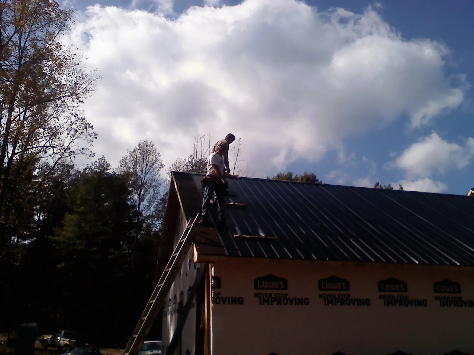 Roofer fastening dark metal panels high against a cloudy sky, from a Roof Inspection job in Irving