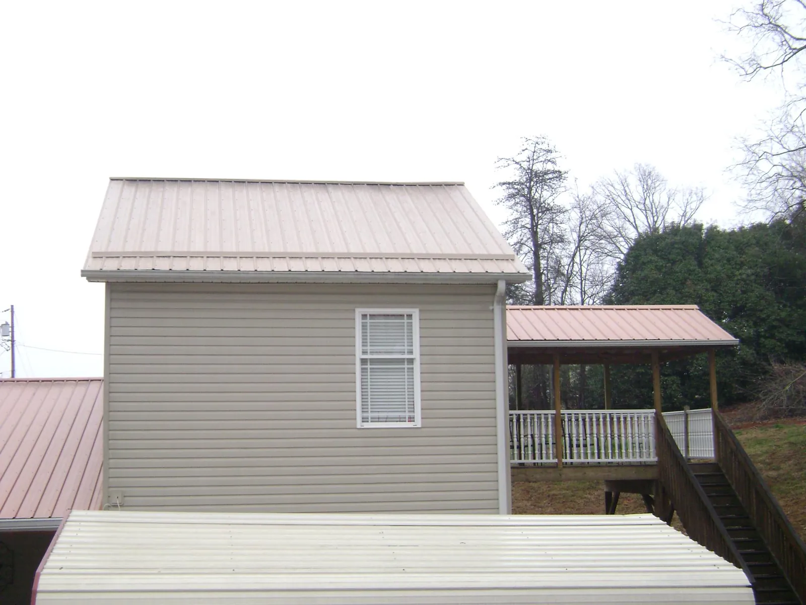 Tan metal roofs on a two story addition and attached porch, from a Roof Replacement job in Irving